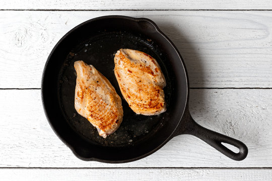 Two whole chicken breasts roasting in cast iron pan isolated on white. Top view.