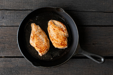 Two whole chicken breasts roasting in cast iron pan isolated on dark wood. Top view.