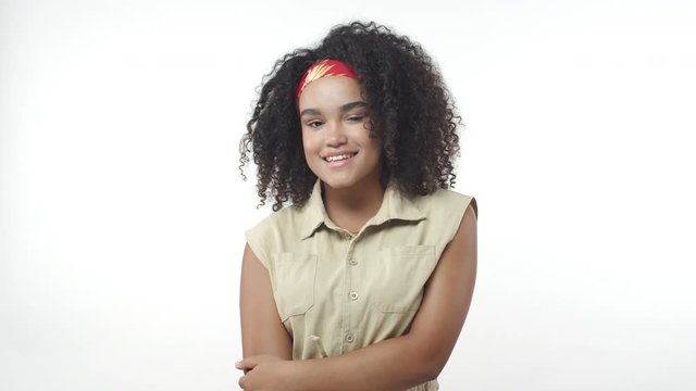 Cheeky, lively and coquettish african-american woman with afro haircut, red headband, standing flirty, smiling, winking camera and move silly on feet, happy looking, slow-motion portrait