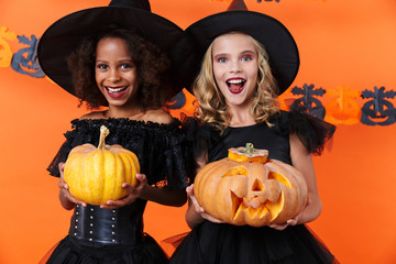 Image of laughing multinational girls holding pumpkins