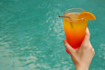 Close up image of woman's hand holding a big cocktail glass next to the swimming pool, summertime vacation leisure activity