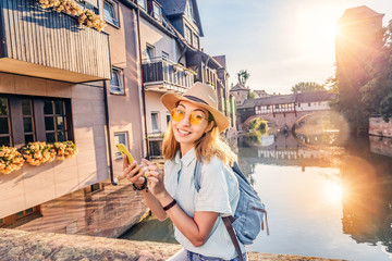 Fototapeta na wymiar Happy asian woman tourist taking photo of the old town of Nurnberg city and Pegnitz river. Travel blogger in Germany concept