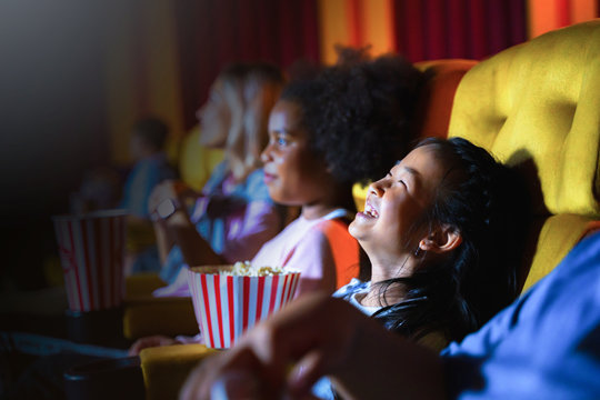 the girl and group of kid are seating and watching the cinema at movie theater seats. The faces have feeling happy and enjoy.