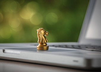 Online strategy, online marketing or business strategy concept. Golden chess knight is on laptop with bokeh background (depth of field photography). © Costello77