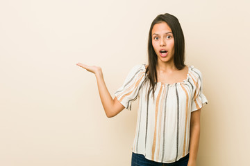 Young hispanic woman impressed holding copy space on palm.