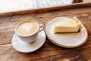 A Cup of cappuccino with foam in the shape of a heart and a piece of cheesecake on a vintage wooden background in a cafe