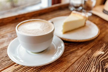 A Cup of cappuccino with foam in the shape of a heart and a piece of cheesecake on a vintage wooden background in a cafe