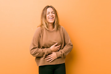 Obraz premium Young authentic charismatic real people woman against a wall laughs happily and has fun keeping hands on stomach.