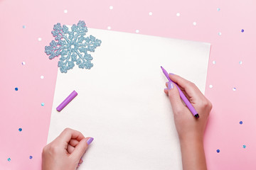 Woman manicured hands holding pen and writing goals and plans for new year. Flat lay on pastel pink...