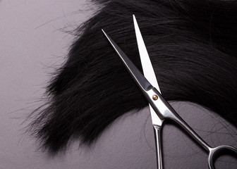 Professional hairdresser scissors lying on natural black hair. Barber scissors and black hair close-up.