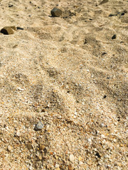 Yellow beach sand with small stones. Footprints in the sand.