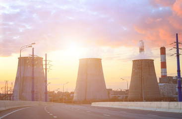 Empty road with thermal power plant and smoke coming from pipes at sunset in big city