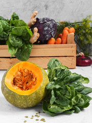 Closeup of a pumpkin with a bunch of fresh spinach. Freshly harvested vegetables in a wooden box (turnips, beets, carrots, greens). Natural organic products.