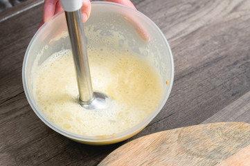 close-up whipping the mixture of homemade mayonnaise with a blender in a plastic bowl