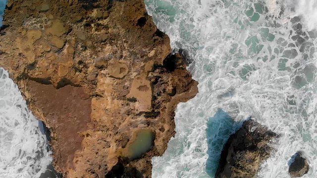 Rocks against ocean waves, overhead super slow motion view from drone