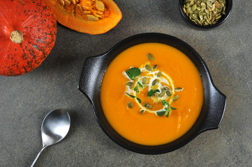 Pumpkin cream soup in a black plate. The soup is decorated with pumpkin seeds and green sprouts. View from above. Close-up.