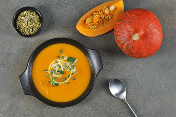 Pumpkin cream soup in a black plate. The soup is decorated with pumpkin seeds and green sprouts. View from above. Close-up.