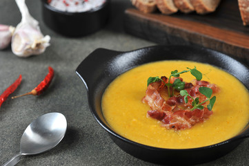 Pea cream soup with bacon. The soup is decorated with green pea sprouts. Dark background. Close-up.