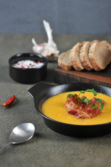 Pea cream soup with bacon. The soup is decorated with green pea sprouts. Dark background. Close-up. The vertical orientation of the frame.