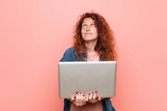 Young caucasian redhead woman holding a laptop smiling confident with crossed arms.