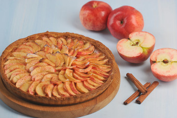 Tart apple pie on a light background. Apples and cinnamon sticks complement the composition. Close-up.