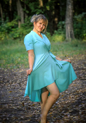 A young blonde woman is walking in a city park in a blue dress.