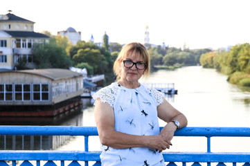 A woman stands on a bridge, against the background of a river.