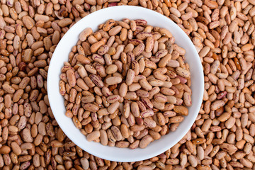 Read bean beans in a white bowl and around on a table in warm light, top view