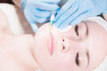 Close-up Attractive young woman gets anti-aging face injections. She lies calmly in a clinic or salon. An experienced young cosmetologist fills female wrinkles with hyaluronic acid from a syringe
