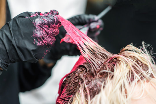 Closeup of the hands of a hairdresser in black gloves dye the hair strand of the client's girl red. Hair coloring process. Beauty and fashion concept.
