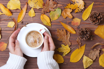 Autumn composition top view. Cup of coffee in the hands and autumn leaves