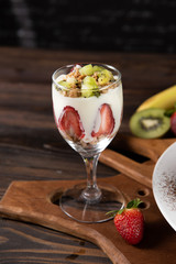 Fresh yogurt with fresh fruit, mixed with crispy cereal, kiwi, strawberry and banana in wine glass. Decorate many fresh fruit on real chopped wood floor. Eat the right amount of sweetness