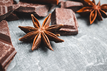 Star anise and chocolate cubes on grey textured background, close-up view