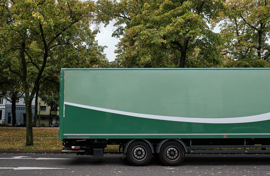 Side view of a green trailer with blank space for graphics in a road with green trees
