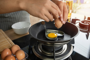 Hands breaking an egg into heart block in a pan