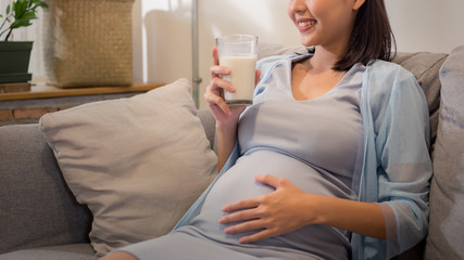 Obraz na płótnie Canvas Young beauty happy Asian pregnant woman holding glass of milk drinking healthy drink.