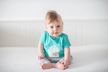 Fototapeta premium Portrait of adorable Caucasian baby girl with blue eyes, looking at the camera calmly, with curiosity, interactivity or inquisitiveness and sitting in a pristine white baby cot while holding her toes