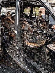 A burnt car interior after a fire or an accident in a parking lot covered with rust and black coal with scattered spare parts around. Robbery, arson, terrorism.