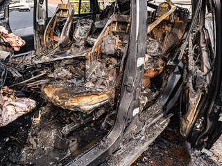 A burnt car interior after a fire or an accident in a parking lot covered with rust and black coal with scattered spare parts around. Robbery, arson, terrorism.