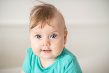 Fototapeta premium Portrait of adorable Caucasian baby girl with blue eyes, looking at the camera calmly, with curiosity, interactivity or inquisitiveness and sitting in a white baby cot; cute baby expressions concepts