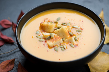 Cream-soup with pumpkin, fried cheese and pumpkin seeds served in a black bowl, close-up, selective focus