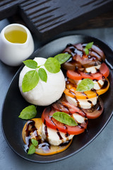 Close-up of caprese salad with tomatoes and mozzarella cheese served on a black plate, vertical shot
