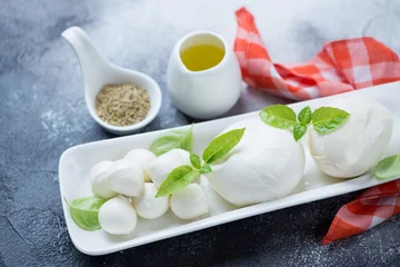 Foto op Plexiglas Closeup of mozzarella cheese with olive oil and green basil leaves, studio shot, selective focus © Nickola_Che