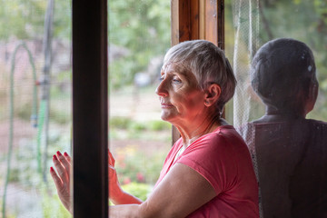 Obraz premium older woman with serious and sad expression looking out the window
