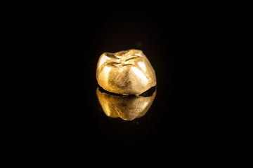 Zahngold: Goldzahn auf schwarzem Untergrund spiegelnd
