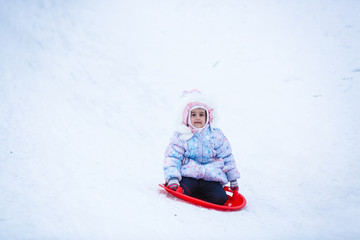 Fototapeta na wymiar Cute litter girl sliding down on the snow mountain