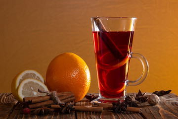 Mulled wine with orange peel, cinnamon sticks and star anise and citrus on a wooden table on an orange background.