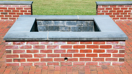 Square brick fire pit with brick wall in background. No fire. 