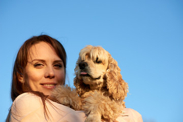 Closeup portrait of slightly blurred young beautiful woman hugging sharp spaniel dog. Clear blue sky background.