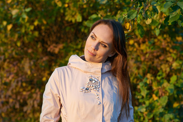 Beautiful young woman wearing light pink coat looking away. Blurry autumn leaves background.